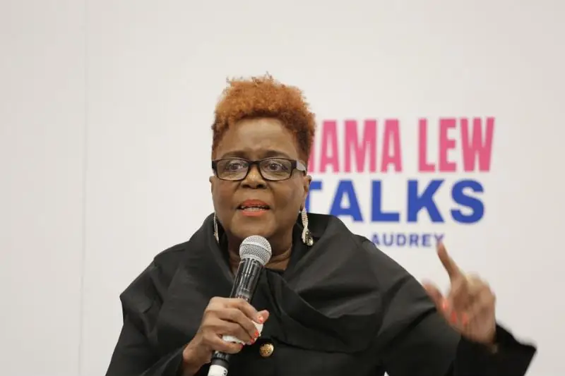 Audrey Lewis speaks into a microphone in front of a Mama Lew Talks sign