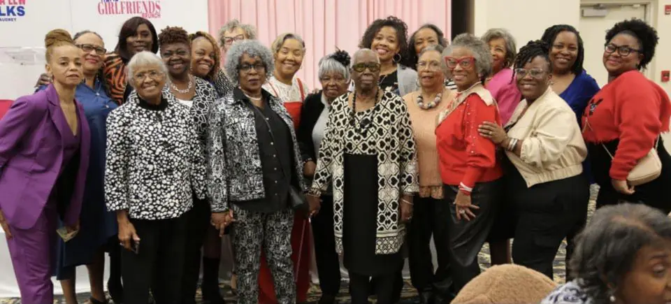 Two dozen women stand together smiling in front of the Real Girlfriends Brunch backdrop