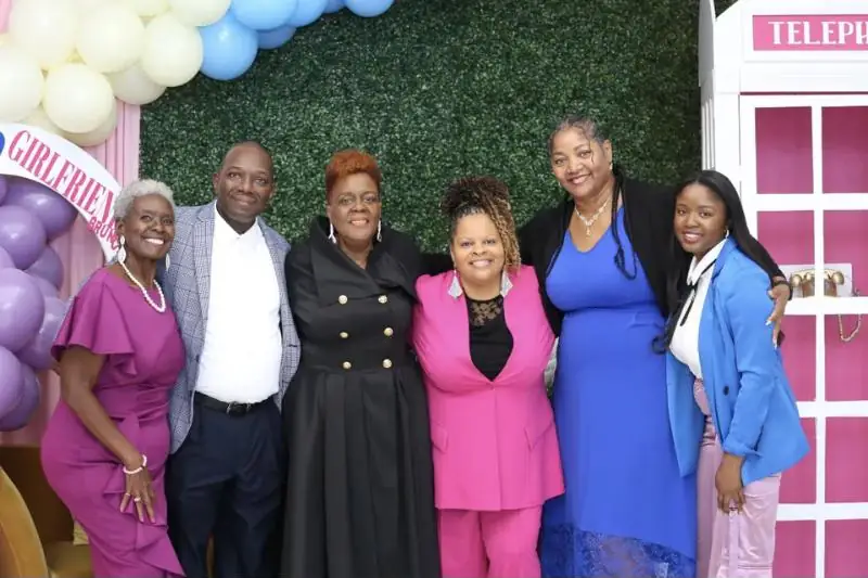 Guests pose together in front of a greenery wall and pink telephone booth